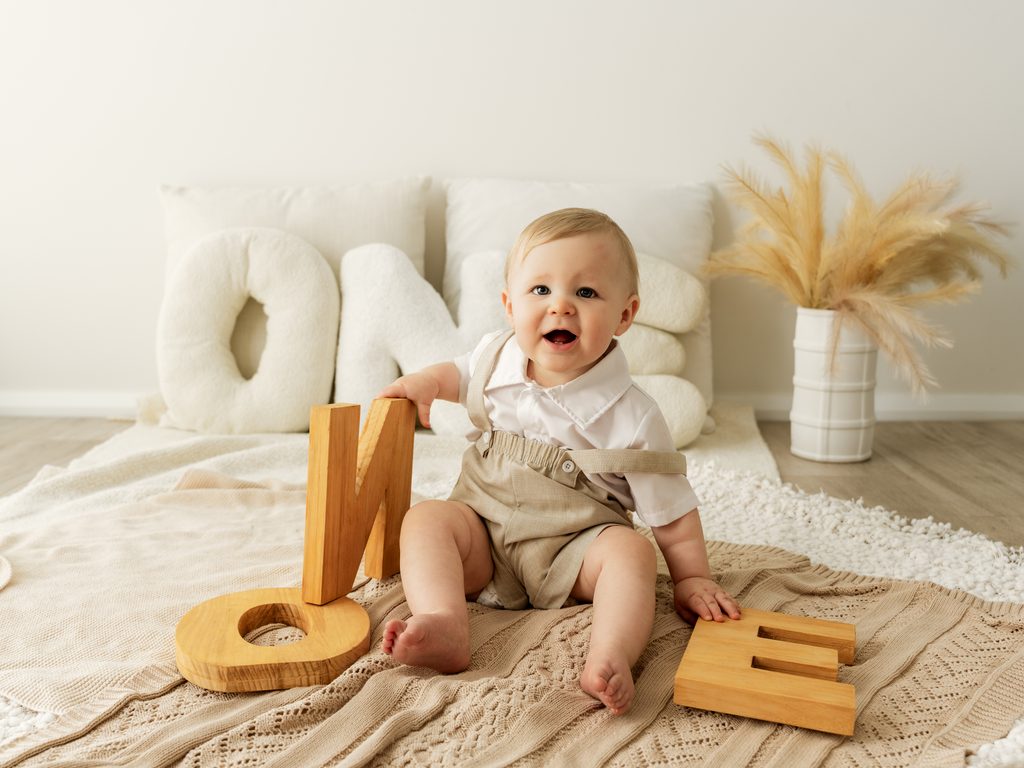 Smiling baby sitting beside wooden ONE letters during a first birthday portrait session at Four O Photography.