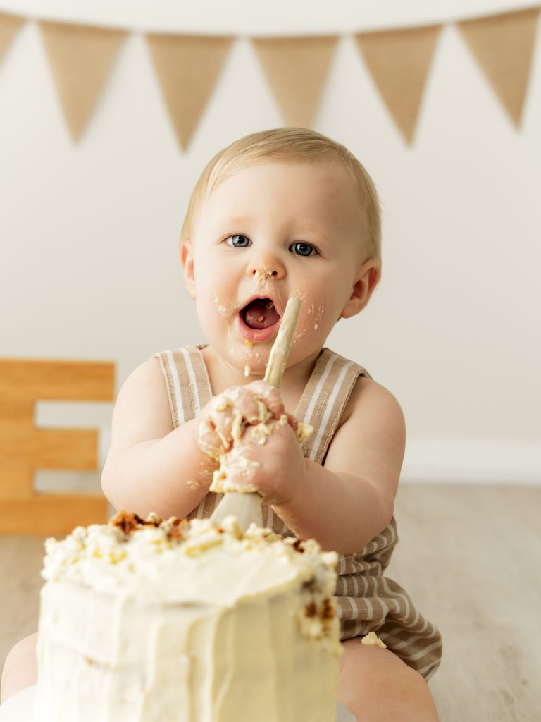One-year-old baby enjoying birthday cake during a neutral-themed cake smash photoshoot in Perth.